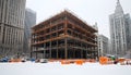 steel frame structure of a building under construction surrounded by snow and tall city skyscrapers in an urban winter setting Royalty Free Stock Photo