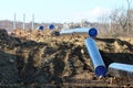 Construction site for new oil pipeline with multiple large diameter pipes and industrial chimneys in background