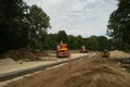 Construction site of new road in city. Yellow tractor and road roller. Green trees in suburban. Royalty Free Stock Photo