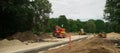 Construction site of new road and sidewalk in city. Yellow tractor and road roller. Green trees in suburban. Royalty Free Stock Photo