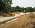 Construction site of new road in suburban. Yellow excavator, road roller and skid loader. Green trees.