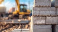 Construction site with stacked concrete blocks in the foreground. An excavator is blurred in the background. Bright sunlight Royalty Free Stock Photo