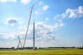 Construction site of a wind turbine, tall crane installing a tube on the tower, nacelle, rotor hub and blades lying still on the Royalty Free Stock Photo