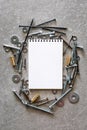 Construction tools. The screws, nuts and bolts arranged around blank spiral bound note book paper on concrete background