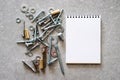 Construction tools. The screws, nuts and bolts arranged around blank spiral bound note book paper on concrete background