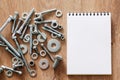 Construction tools. The screws, nuts and bolts arranged around blank spiral bound note book paper on wooden background