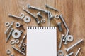 Construction tools. The screws, nuts and bolts arranged around blank spiral bound note book paper on wooden background