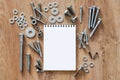 Construction tools. The screws, nuts and bolts arranged around blank spiral bound note book paper on wooden background