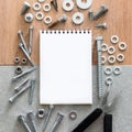 Construction tools. The screws, nuts and bolts arranged around blank spiral bound note book paper on wooden and concrete