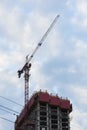 Construction tower crane next to a building under construction against the background of the blue sky with clouds Royalty Free Stock Photo