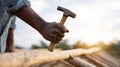 Construction worker assembling wooden roof structure with hammer in bright sunlight, trees and sky in background Royalty Free Stock Photo