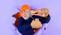 Construction worker or builder in hard hat with adjustable wrench looking through paper hole. Bearded man in uniform Royalty Free Stock Photo