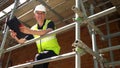 Construction worker on building site standing on scaffolding nodding to camera