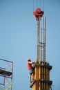 A construction worker controls the crane movement when assembling building blocks against a blue sky