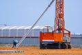 Construction worker with crawler pile driver machine lifting concrete piling for install industrial building structure