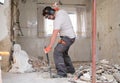 Construction worker digging up the house floor, lifting up old tiles with a crowbar and a hammer