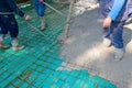 Rigger holding pump hose to pouring fresh concrete, other worker is using hook to pull up square reinforcing steel bars