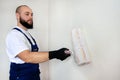 Construction worker doing finish renovation at apartment. Professional painter using white paint roller brush painting of wall. Royalty Free Stock Photo