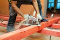 Construction worker with electrical circular saw saws wooden block and a lot of saw dust in apartment is inder