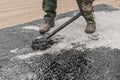 A construction worker is engaged in dirty manual work to repair and apply black bitumen waterproofing tar to the concrete surface