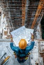 Construction Worker Examining Blueprints Amidst Scaffolding and Cranes at Building Site Royalty Free Stock Photo