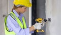 Construction worker in green reflective safety vest and hardhat use a yellow cordless electric drill with battery to drill holes