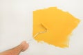 Construction worker doing finish renovation at apartment. Painter using paint roller brush painting of wall with yellow color.