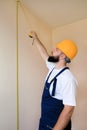 Construction worker and handyman is working on renovation of apartment. Builder is measuring wall of room using measure tape. Royalty Free Stock Photo