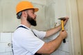 Construction worker and handyman with yellow hammer strikes and nails a nail into wooden wall of kitchen door at construction site Royalty Free Stock Photo