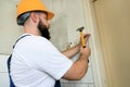 Construction worker and handyman working on renovation work. Builder with yellow hammer strikes and nails a nail into wooden wall. Royalty Free Stock Photo