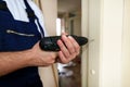 Construction worker and handyman works on renovation of apartment. Builder with electric drill drills nail hole into wall door.