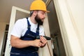 Construction worker and handyman works on renovation of apartment. Builder with electric drill drills nail hole into wall door.