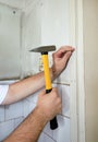 Construction worker and handyman with yellow hammer strikes and nails a nail into wooden wall of kitchen door at construction site Royalty Free Stock Photo