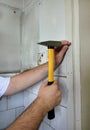 Construction worker and handyman with yellow hammer strikes and nails a nail into wooden wall of kitchen door at construction site Royalty Free Stock Photo