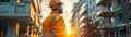 Construction worker in a hard hat and reflective vest overseeing building projects at sunrise in an urban area Royalty Free Stock Photo