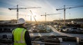 Construction worker in hard hat and safety vest overlooking a bustling building site with cranes at sunset Royalty Free Stock Photo