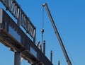 Construction worker, with the help of a mobile telescopic crane, builds the metal structure of an elevated infrastructure
