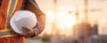 The construction worker holding a hard hat at a job site during sunrise. AI generated image Royalty Free Stock Photo