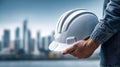 A construction worker holding a white hard hat against a blurred cityscape backdrop. Royalty Free Stock Photo