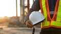 A construction worker holding a white hard hat wearing a safety vest at a construction site Royalty Free Stock Photo