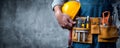 Construction worker holding yellow helmet with tool belt full of tools, ready for work with confident posture Royalty Free Stock Photo