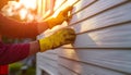 Construction worker installing siding on a house during sunset. The worker wears yellow gloves and red overalls Royalty Free Stock Photo