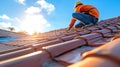 Construction worker installing tile roofing with safety gear at sunset. Royalty Free Stock Photo
