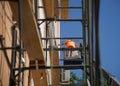 Construction worker-plasterer in a cradle lift and scaffolding next to the outer wall and windows of a multi-storey building. Work