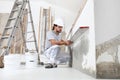 Construction worker plasterer man looks at the spirit level and checks the wall in building site of home renovation with tools and Royalty Free Stock Photo