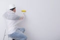 A construction worker in protective clothing and a hard hat, smoothes the wallpaper on the white wall with a special roller, there