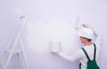 A construction worker in protective clothing and a helmet, applies paint with a roller and holds a bucket in his hand, next to a Royalty Free Stock Photo