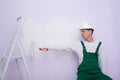 A construction worker in protective clothing, holding out his hands with a roller for applying paint to the wall