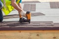 Construction worker putting the asphalt roofing shingles with nail gun on a new frame house.