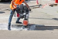 A construction worker is ramming a trench with a vibrating rammer at a construction site and kicking up a cloud of dust around him